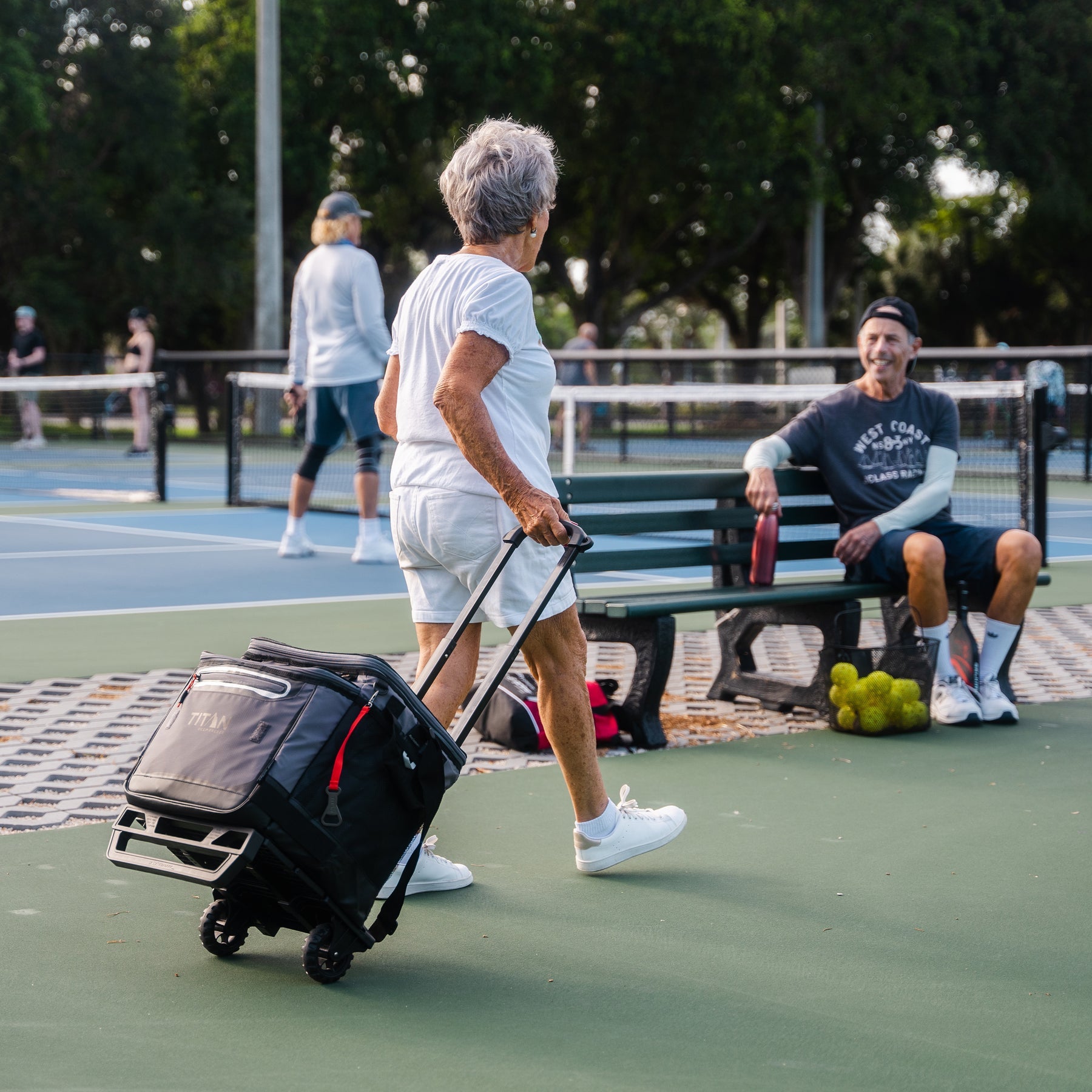 Person with a Titan wheeled cart on a tennis court with others in the background