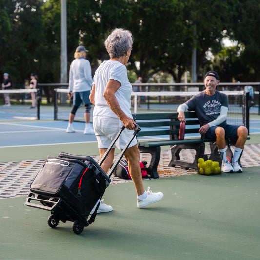 Person with a Titan wheeled cart on a tennis court with others in the background