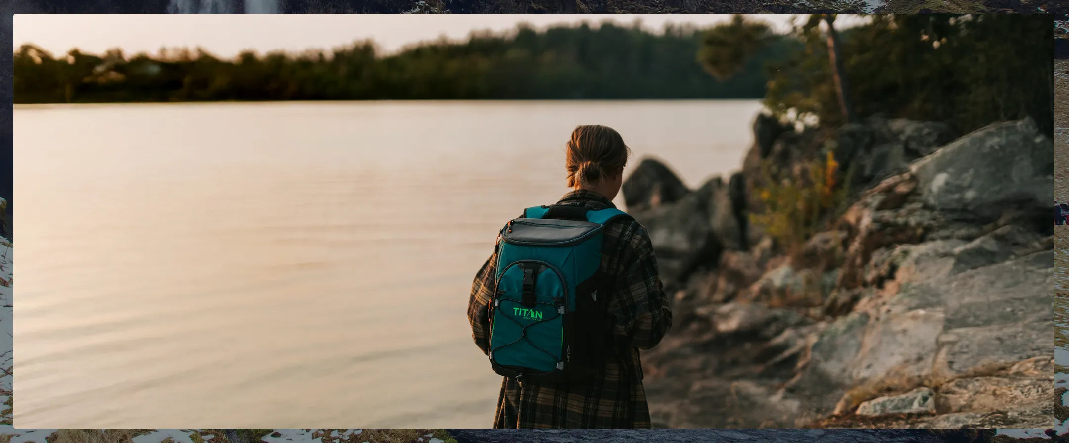 Person with a blue backpack standing by a lake at sunset