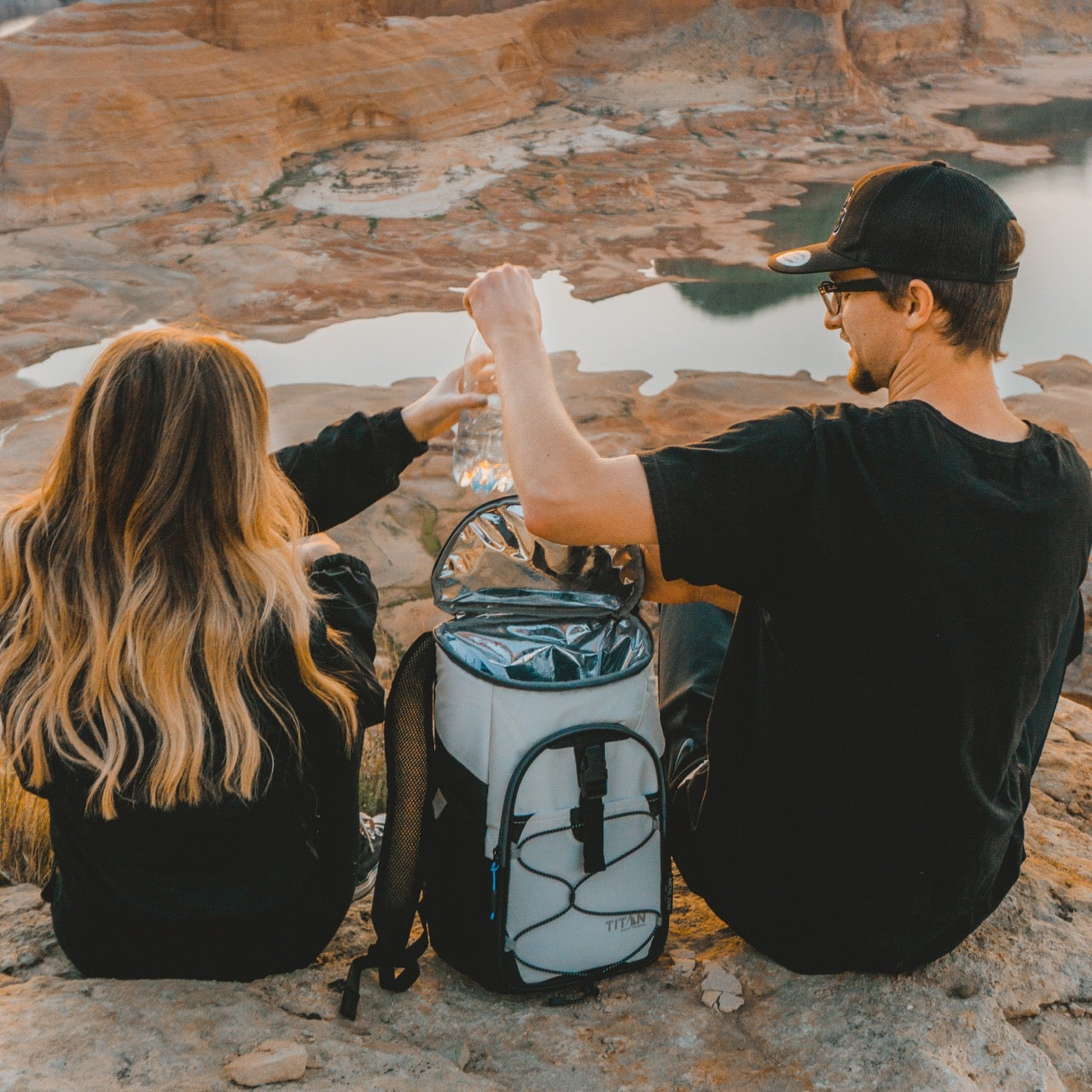 couple sitting on mountain with Titan 24 can cooler backpack